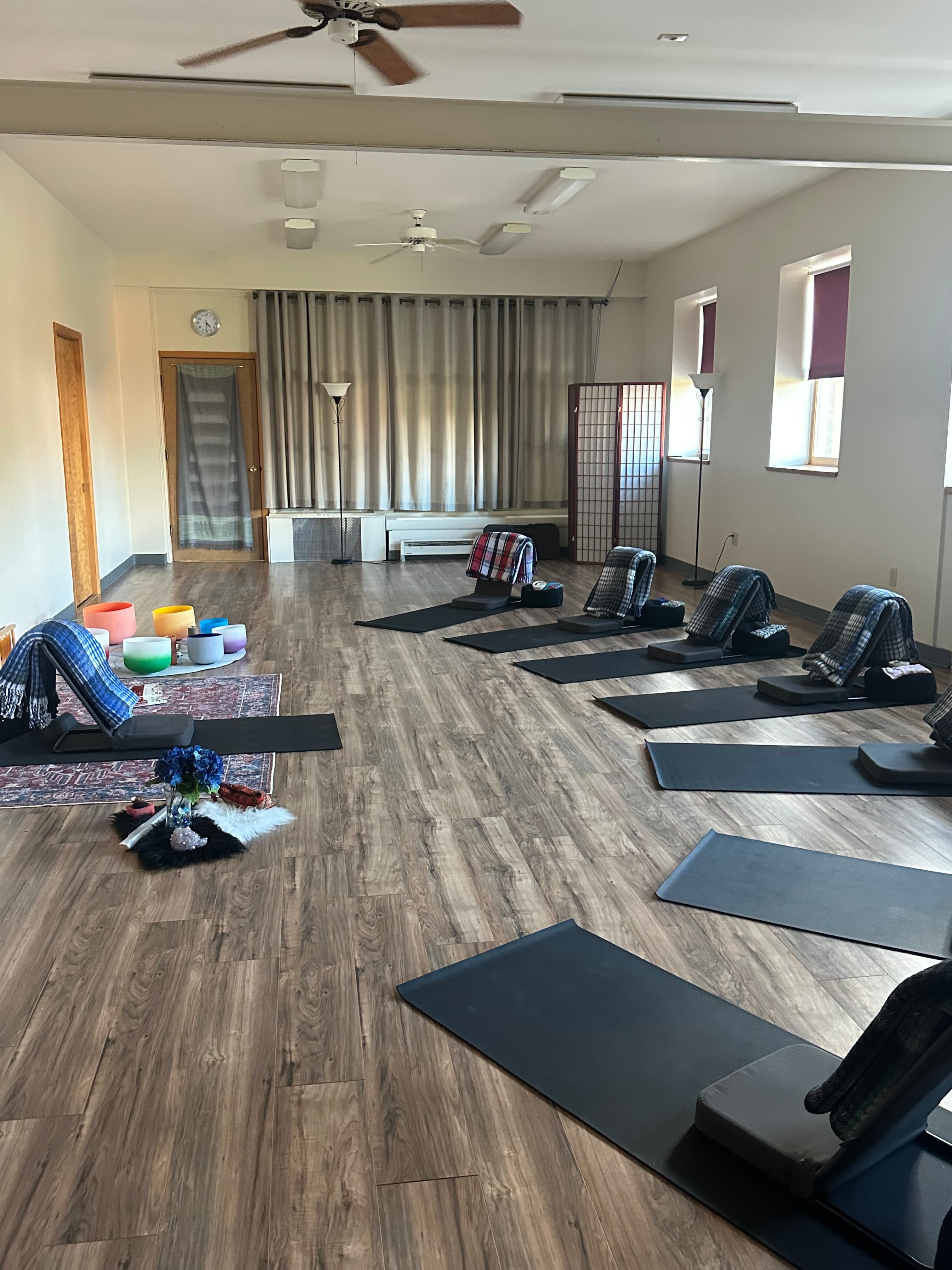 Serene meditation room with yoga mats, backrests, and blankets facing colorful crystal singing bowls.